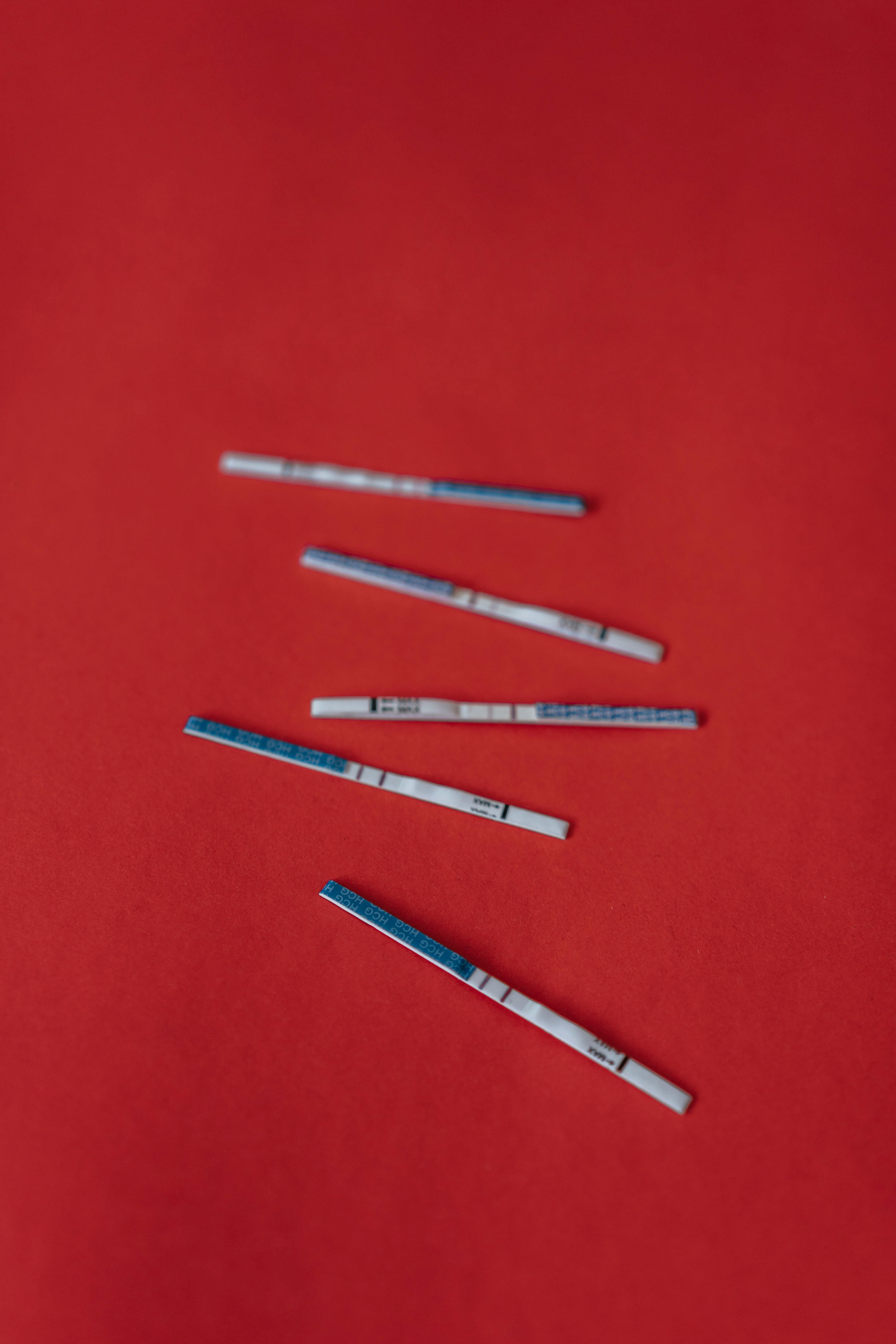 Five pregnancy test strips placed on a vibrant red background, indicating fertility analysis.