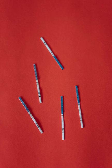 Multiple pregnancy test strips scattered on a vibrant red backdrop, symbolizing fertility and anticipation.