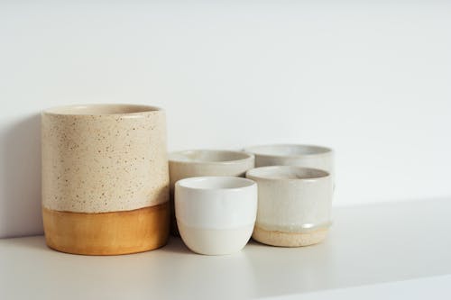 Collection of white and beige ceramic cups placed on shelf in light kitchen