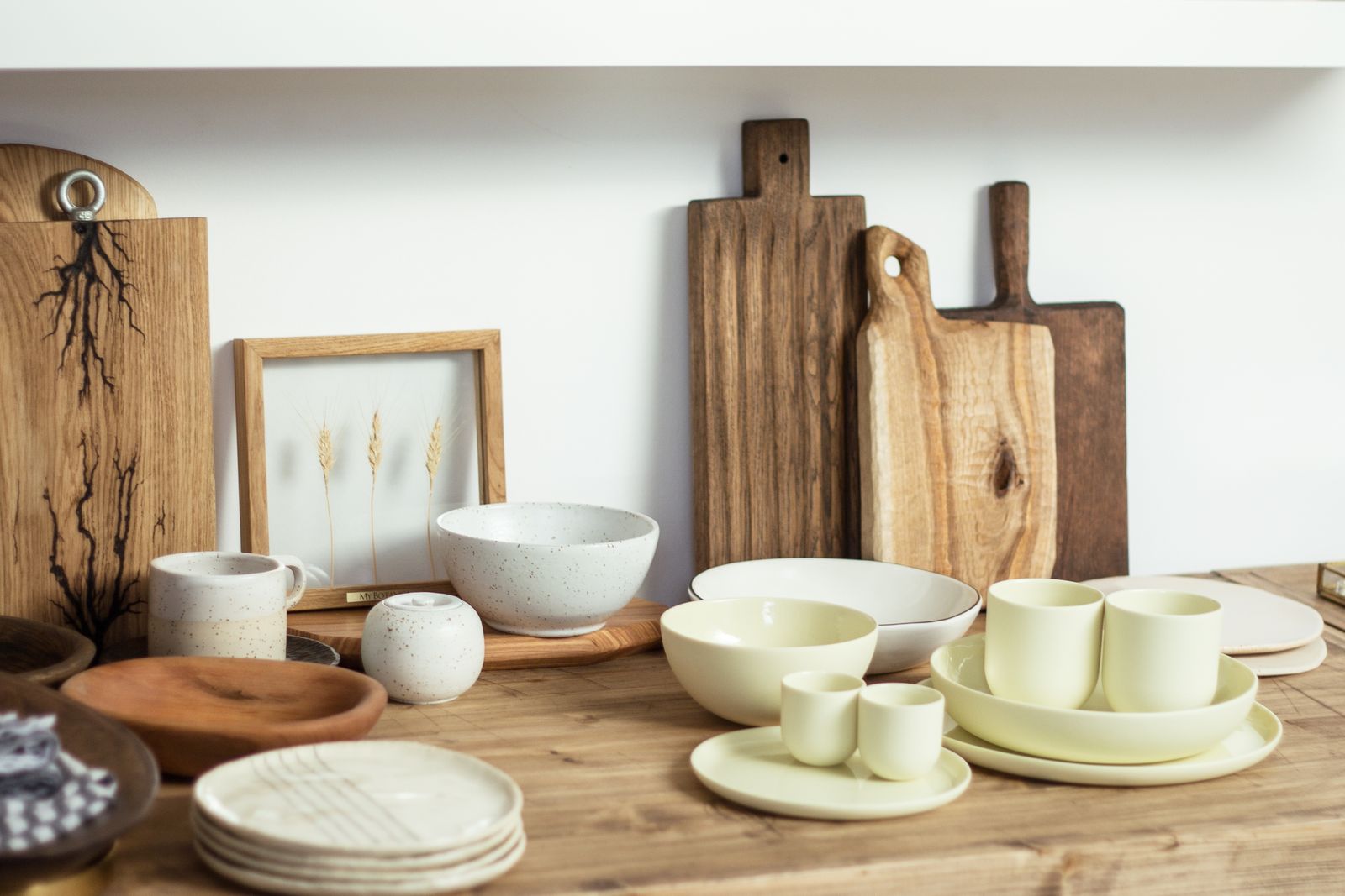 Set of minimalist light ceramic dishware and cutting boards arranged on wooden shelf in modern kitchen