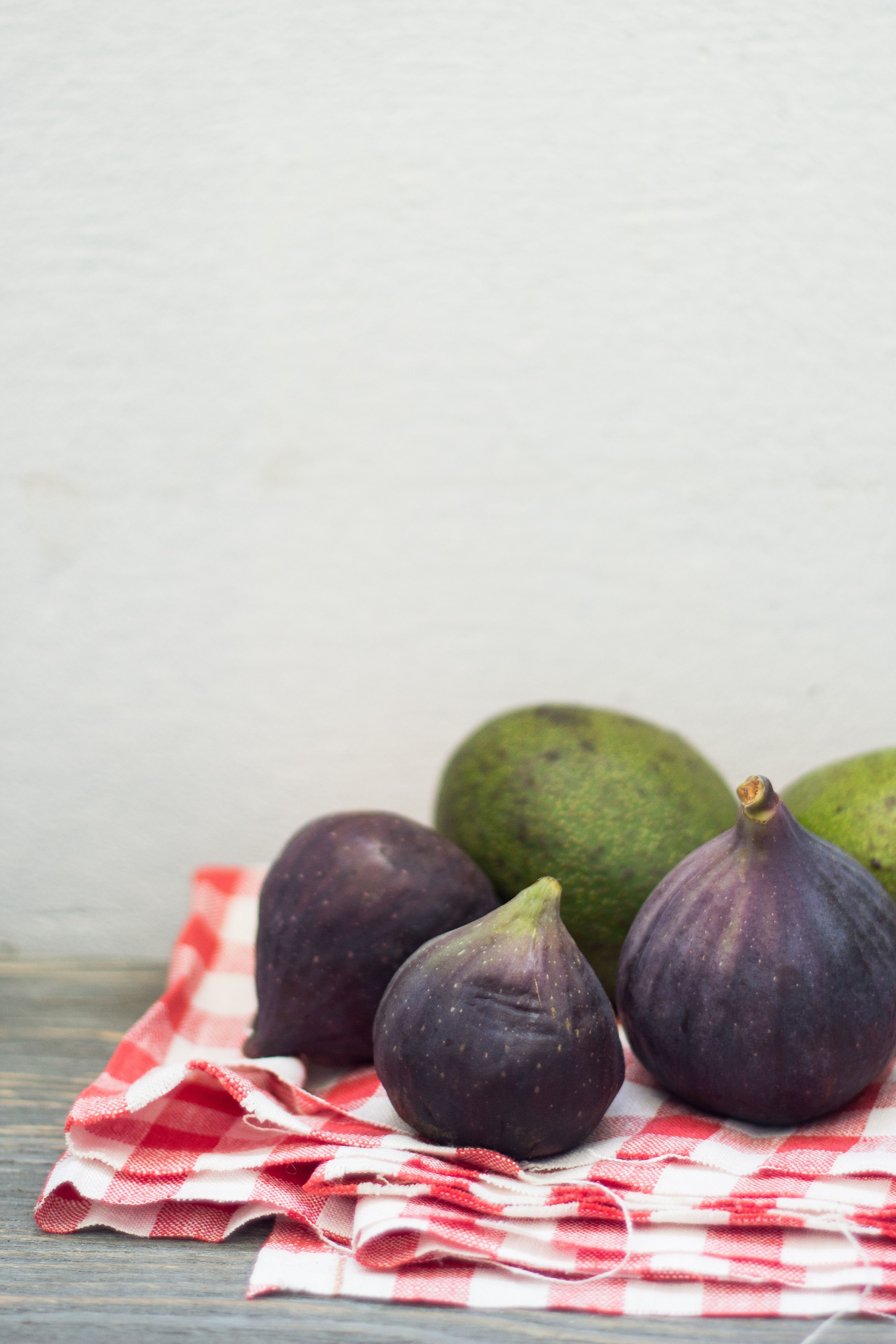 Fotomural Primer plano de higos frescos y aguacates sobre una tela de cuadros rojos, perfecto para fotografía de alimentos.