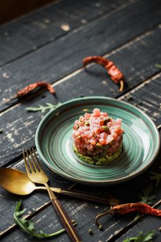 A delicious top view of salmon tartare served on a ceramic plate with rustic cutlery.