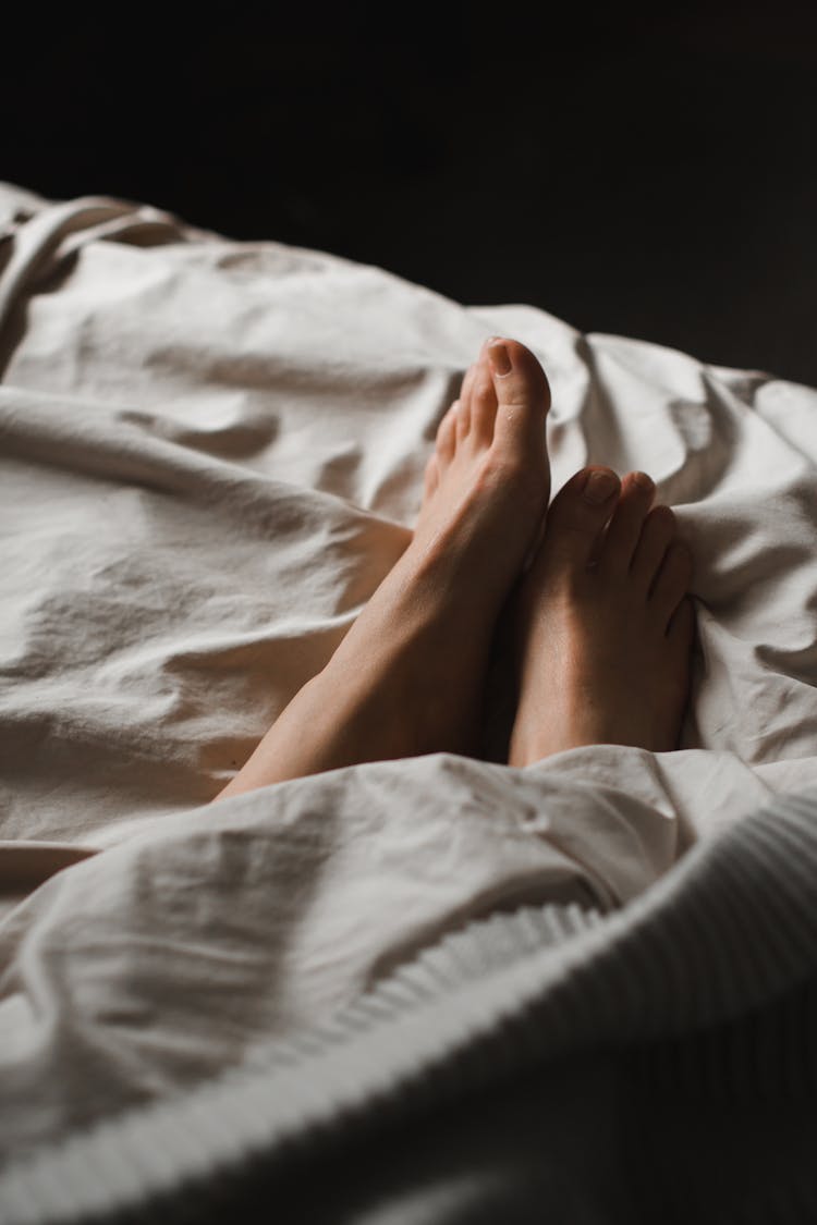 Crop Unrecognizable Female Feet Lying In Cozy Bed