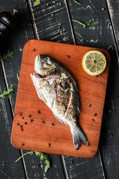 Grilled fish displayed on a wooden board with a lemon slice, ideal for food photography.