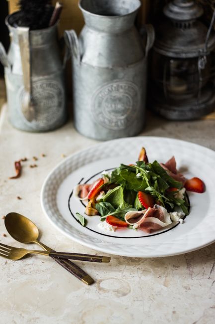 Delicious mixed green salad with prosciutto, strawberries, on rustic setup.