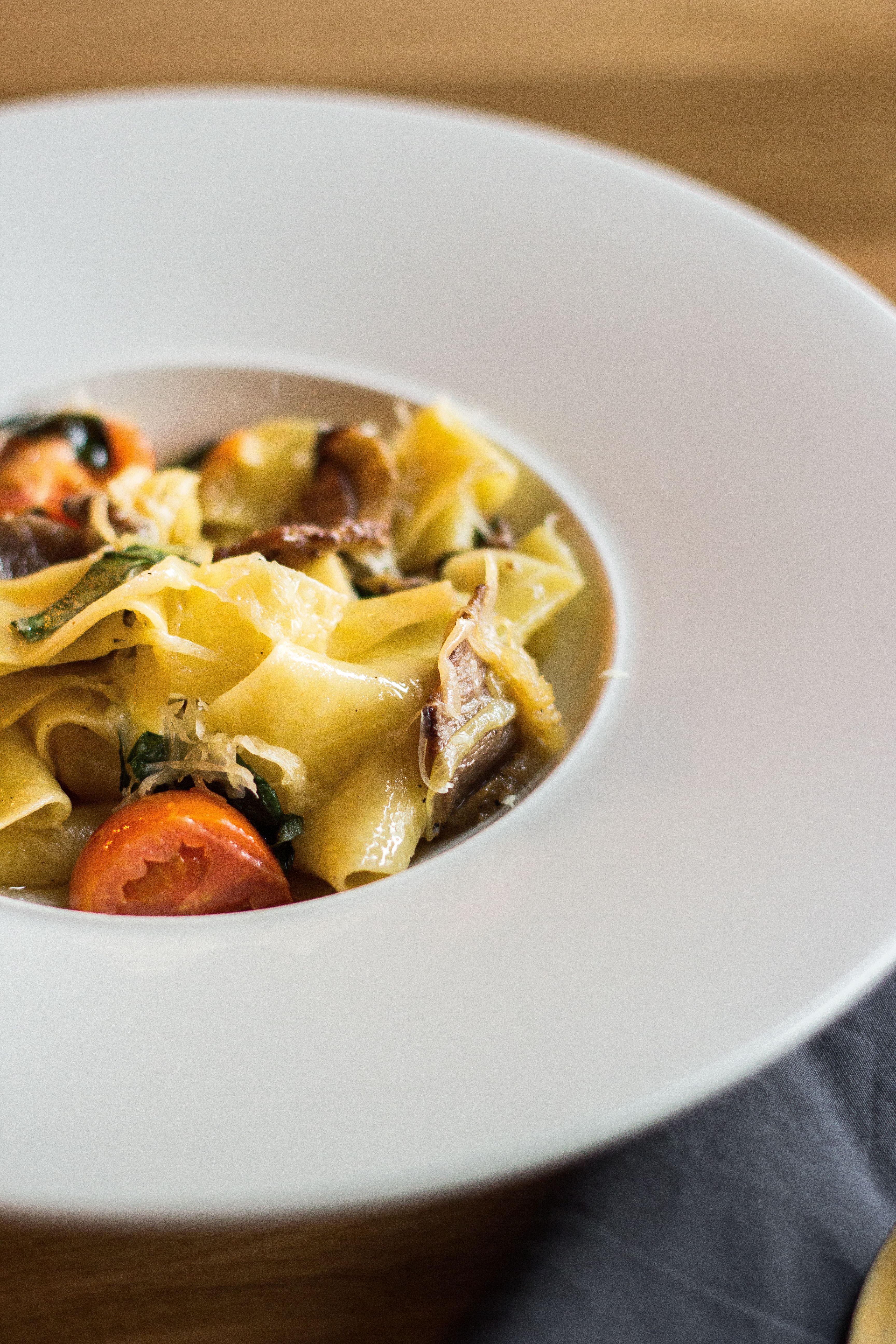 Delicious close-up of pappardelle pasta with tomatoes, spinach, and mushrooms on white plate.