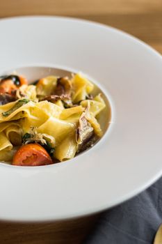 Delicious close-up of pappardelle pasta with tomatoes, spinach, and mushrooms on white plate.