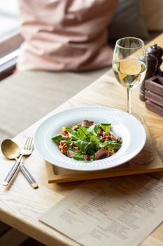 Delicious gourmet salad served with white wine in a cozy restaurant setting, perfect for a refined dining experience.