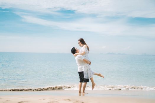 Side view of young happy man lifting girlfriend while spending holiday on beach in sunny day