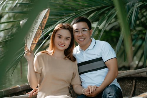 Free Happy Asian couple in casual clothes with coolie hat sitting on boat in river on date and holding hands while looking at camera near green palms in daytime Stock Photo