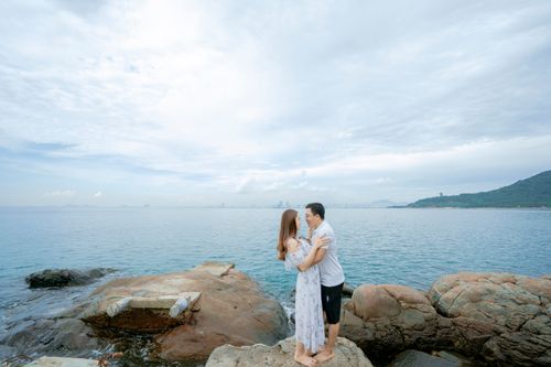 Free Side view full body of barefoot couple in summer clothes cuddling on big boulders on beach near sea in summer day under cloudy sky while looking at each other Stock Photo