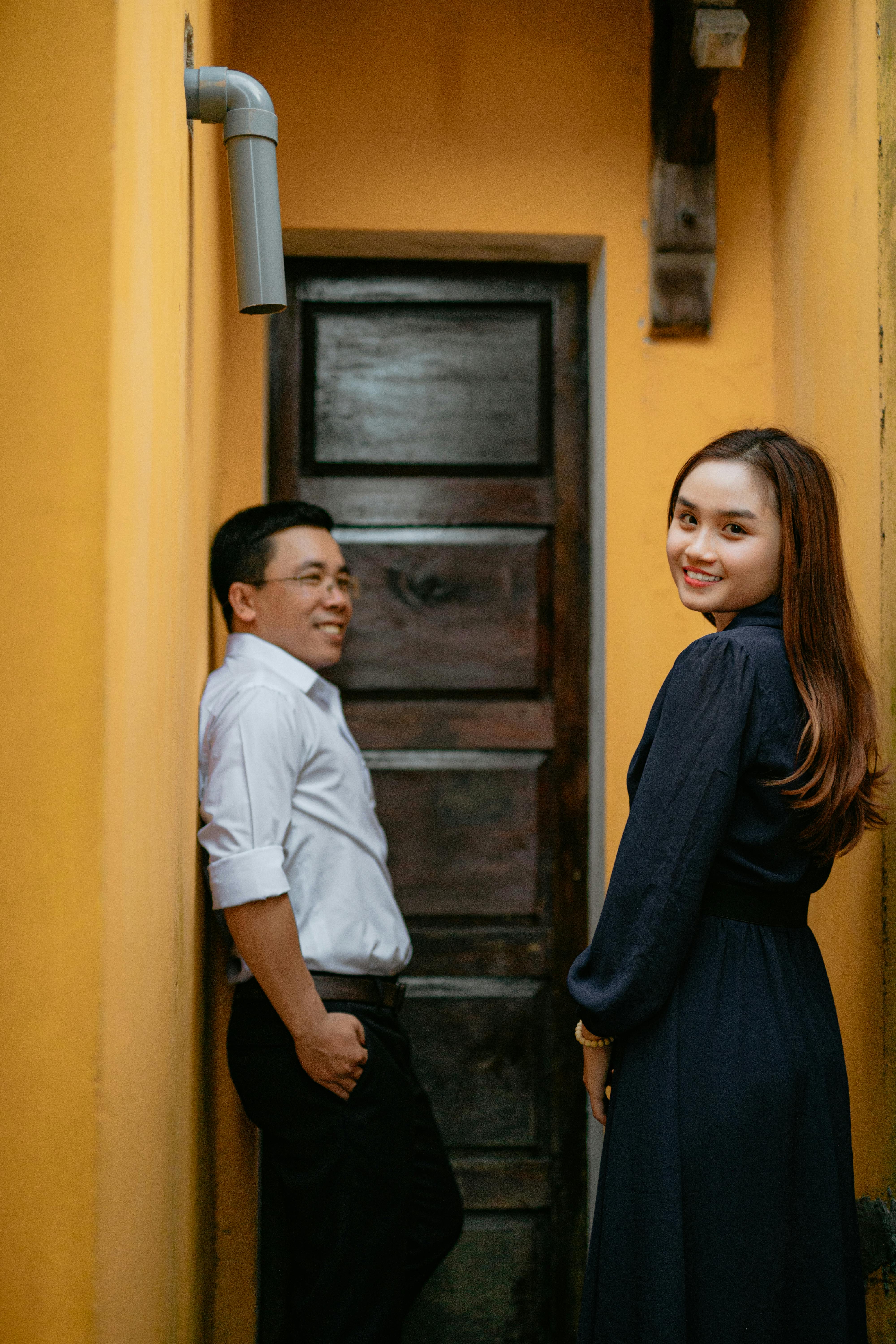 A joyful Asian couple sharing a moment in a narrow, elegant corridor.