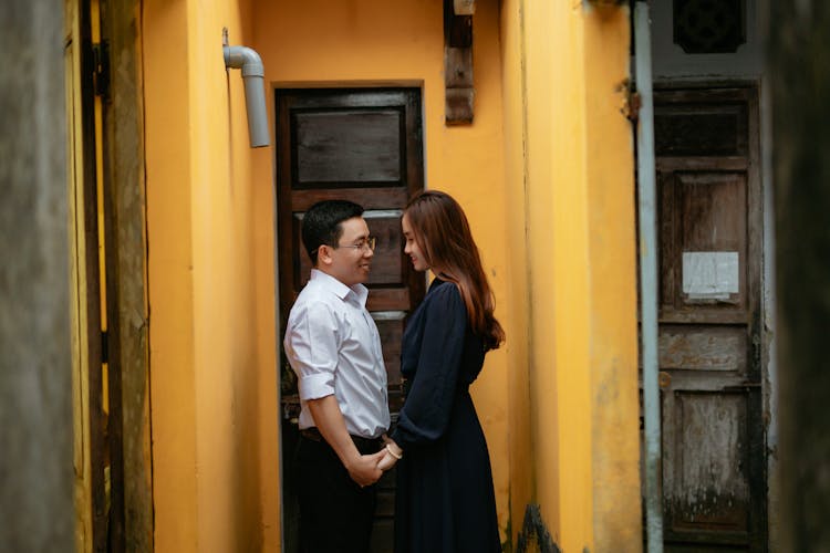 Cheerful Asian Couple Holding Hands Between Old House Walls