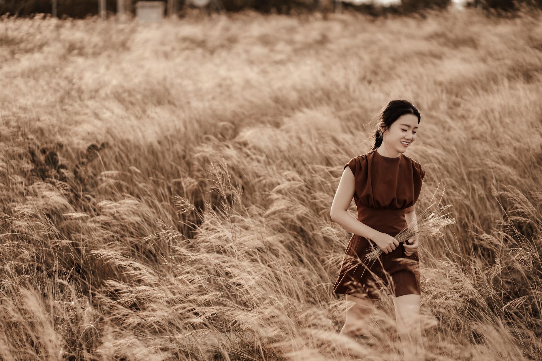 Smiling ethnic woman walking among grass in field · Free Stock Photo