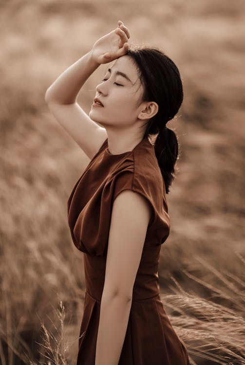 Free Side view of young dreamy Asian female in elegant clothes with closed eyes on meadow on blurred background Stock Photo