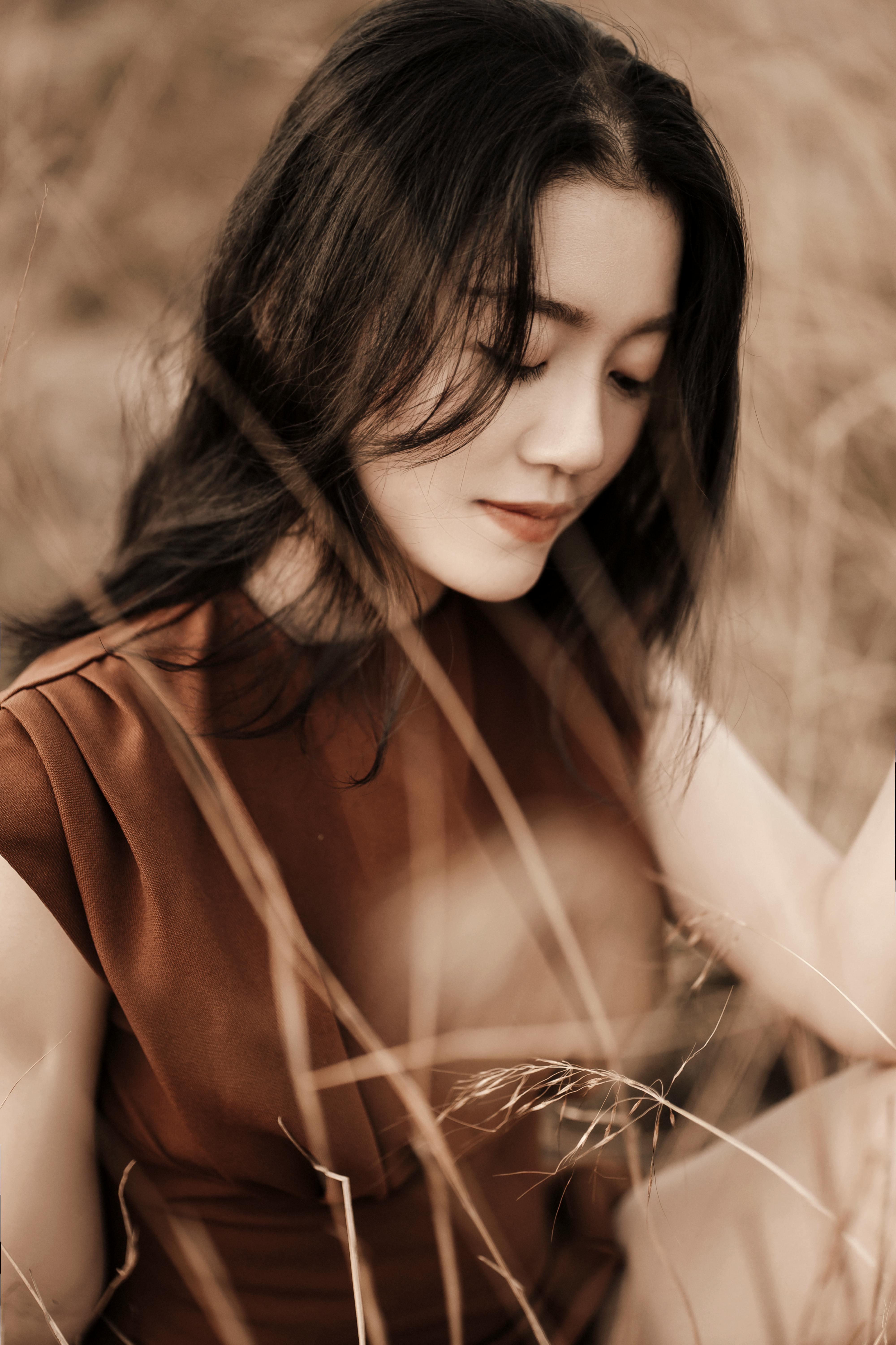 Charming mindful ethnic female with makeup in brown apparel among faded grass in countryside