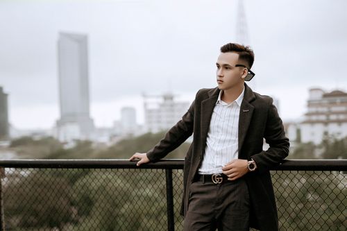 Free Young well dressed ethnic male in modern wristwatch and coat looking away near grid fence in town Stock Photo