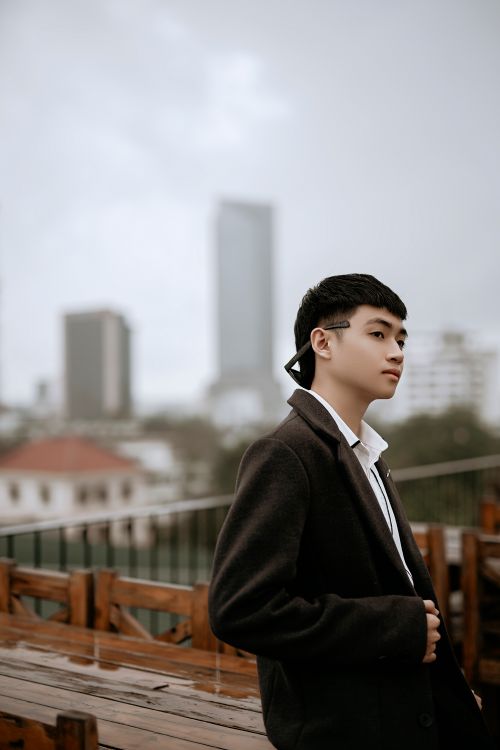 Free Side view of young pensive Asian male in stylish wear looking away on cafeteria veranda in city Stock Photo