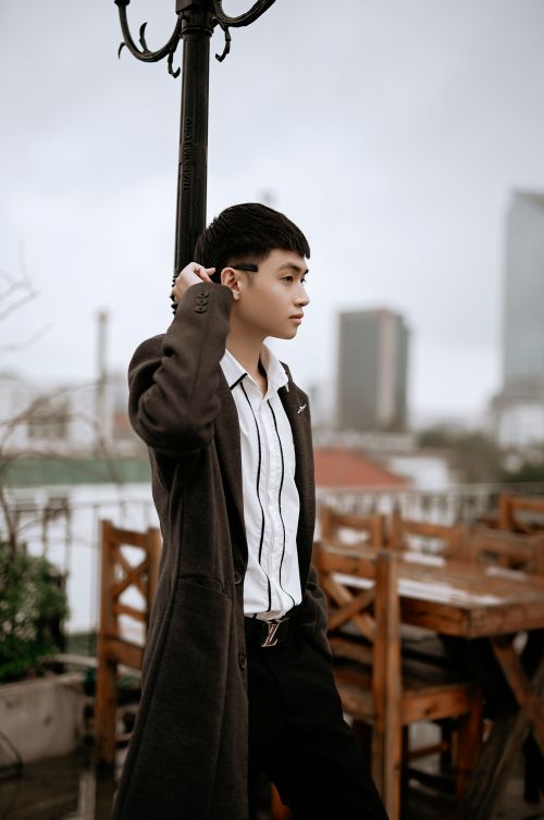 Free Young thoughtful ethnic male in striped shirt and coat looking away near post on cafe terrace in city Stock Photo