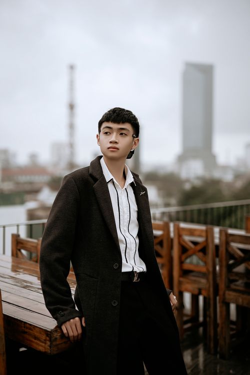 Free Young wistful Asian male in coat and striped shirt looking away on cafe veranda in city Stock Photo