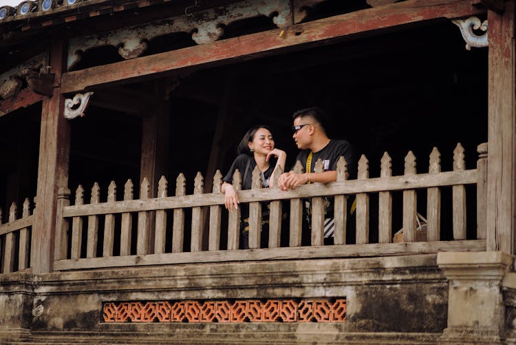 Smiling Asian Couple Talking On Veranda Of Old House