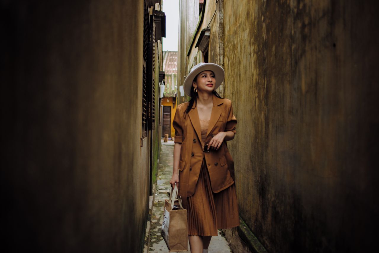 young content ethnic female in trendy outfit strolling on narrow urban