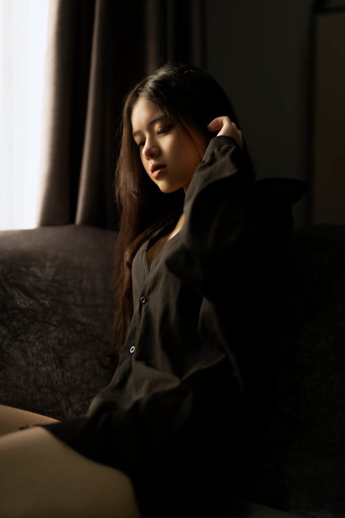 Dreamy Asian woman touching hair and sitting on sofa