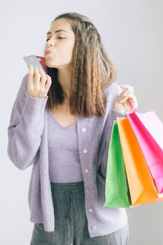 Woman playfully kissing credit card with colorful shopping bags in hand.
