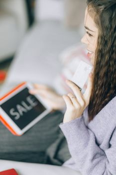 Woman holding a credit card and tablet with 'Sale' for online shopping.