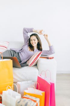 Woman comfortably shopping online with multiple bags around her.
