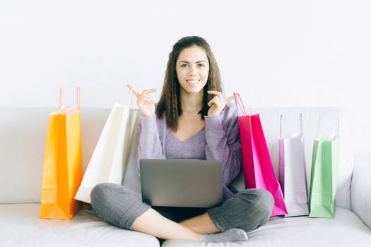 Woman sitting on a couch with shopping bags, smiling while using a laptop for online shopping.
