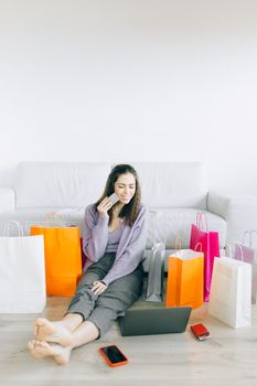 Young woman enjoys online shopping surrounded by colorful paper bags at home.