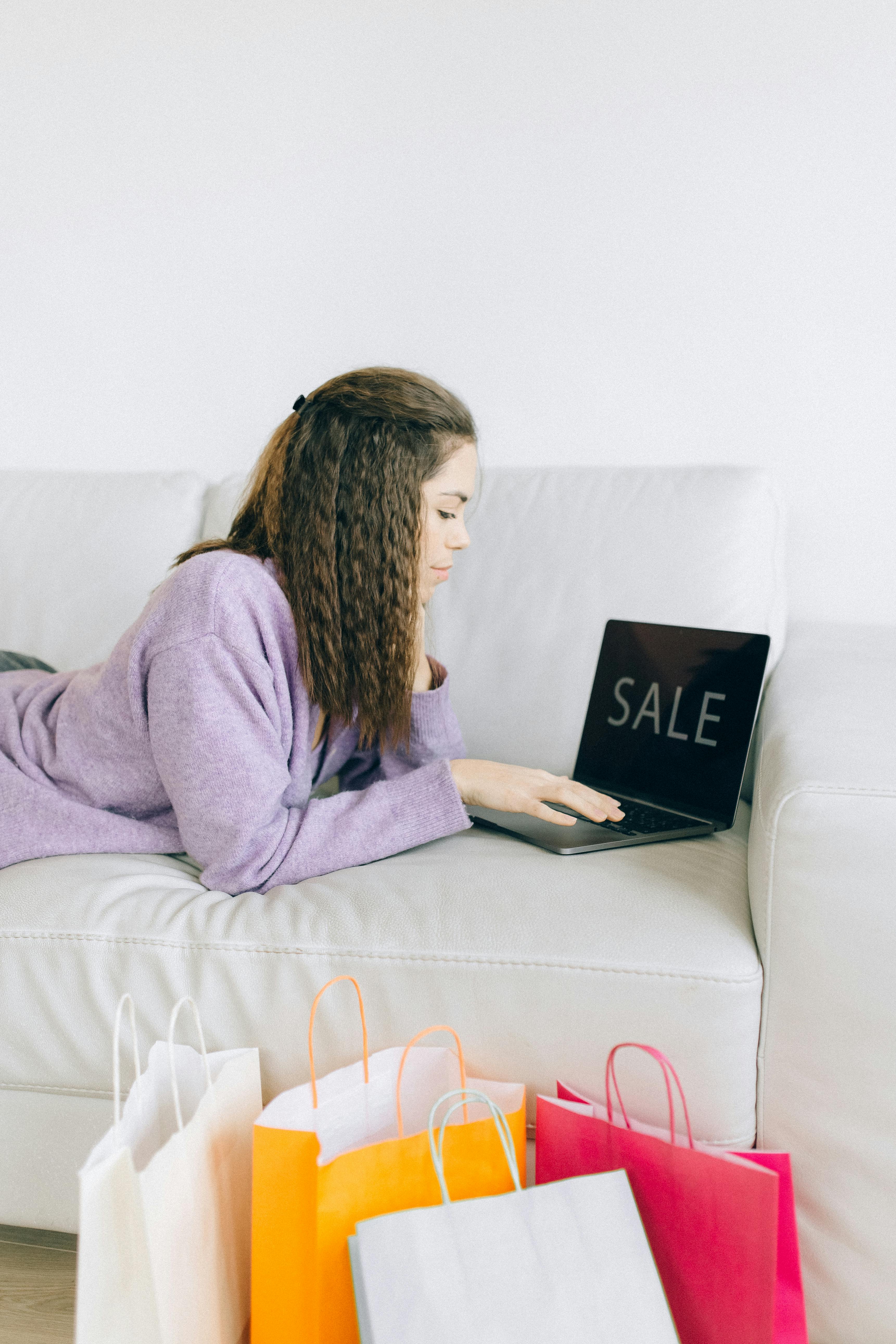 a woman using her laptop while lying on a sofa