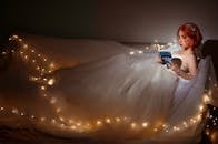 Asian bride reading book on bed with glowing garland