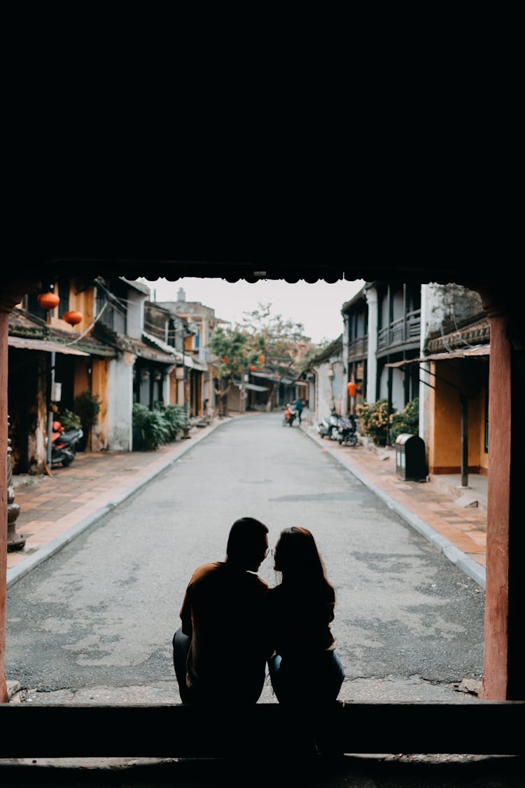 Silhouette Of Couple Sitting On Street In Residential District In Tropical Town