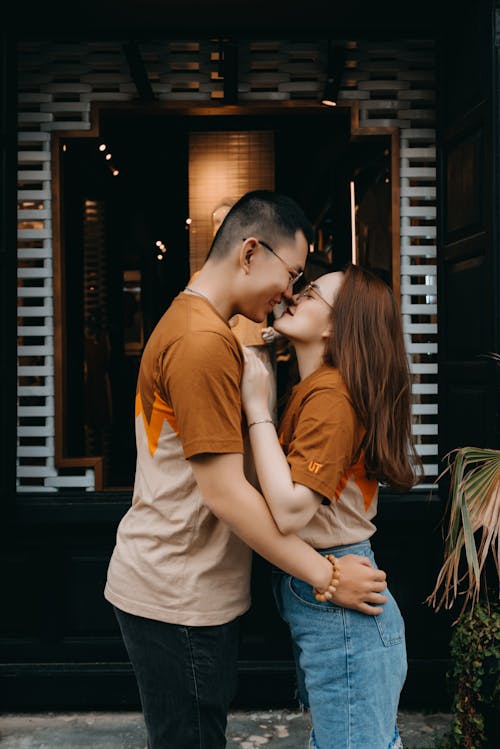 Glad Asian couple kissing and cuddling near modern building