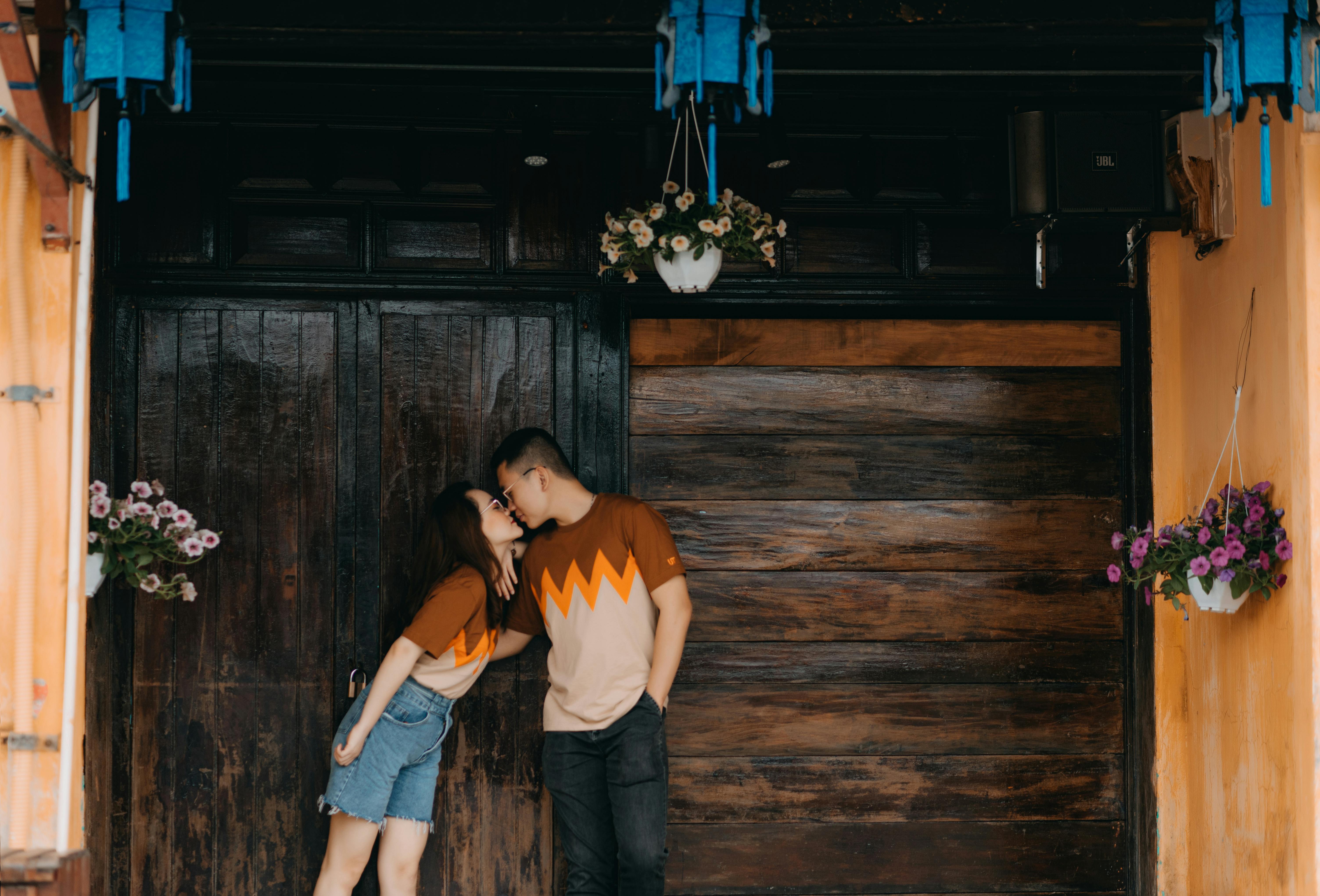 Satisfied ethnic couple in casual same outfit kissing near wooden door while spending time together in city at daytime