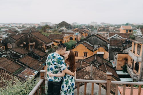 Free Back view of satisfied Asian couple in same clothes standing on terrace of rooftop while hugging and kissing in gloomy day Stock Photo