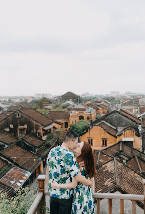 From above of young ethnic couple in same summer clothes standing on rooftop terrace while kissing and hugging at daytime