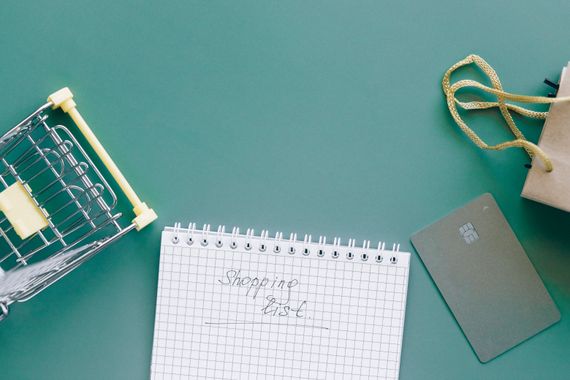 Pessoa escrevendo lista de compras no papel com planejamento semanal