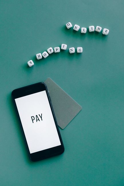 Smartphone with the word 'Pay' displayed alongside a card and letters spelling 'Shopping Online' on a green background.