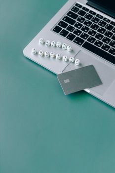 Minimalistic image of a laptop, bank card, and text spelling 'online shopping' on a green background.