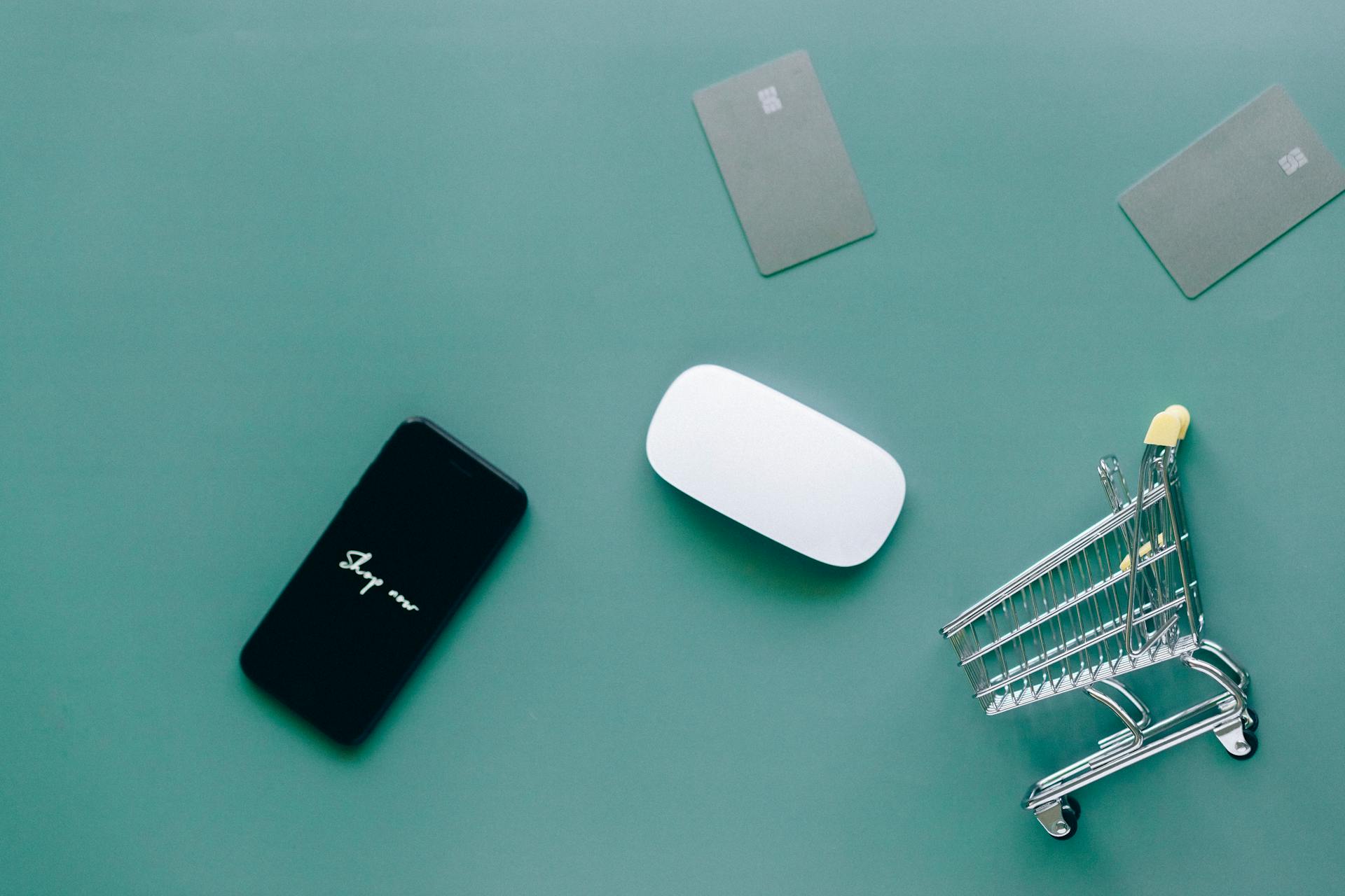 Flat lay of smartphone, cards, and shopping cart on green. Perfect for e-commerce and online shopping themes.