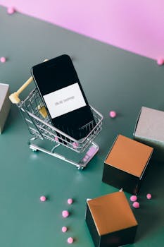 Conceptual image of online shopping with a smartphone in a miniature cart.
