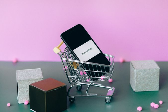 A smartphone with a shopping cart depicting the concept of online shopping in a colorful studio setup.