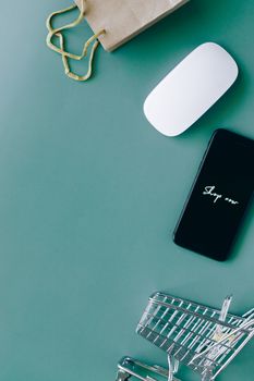 Flat lay of a smartphone, shopping cart, and paper bag representing online shopping and e-commerce.