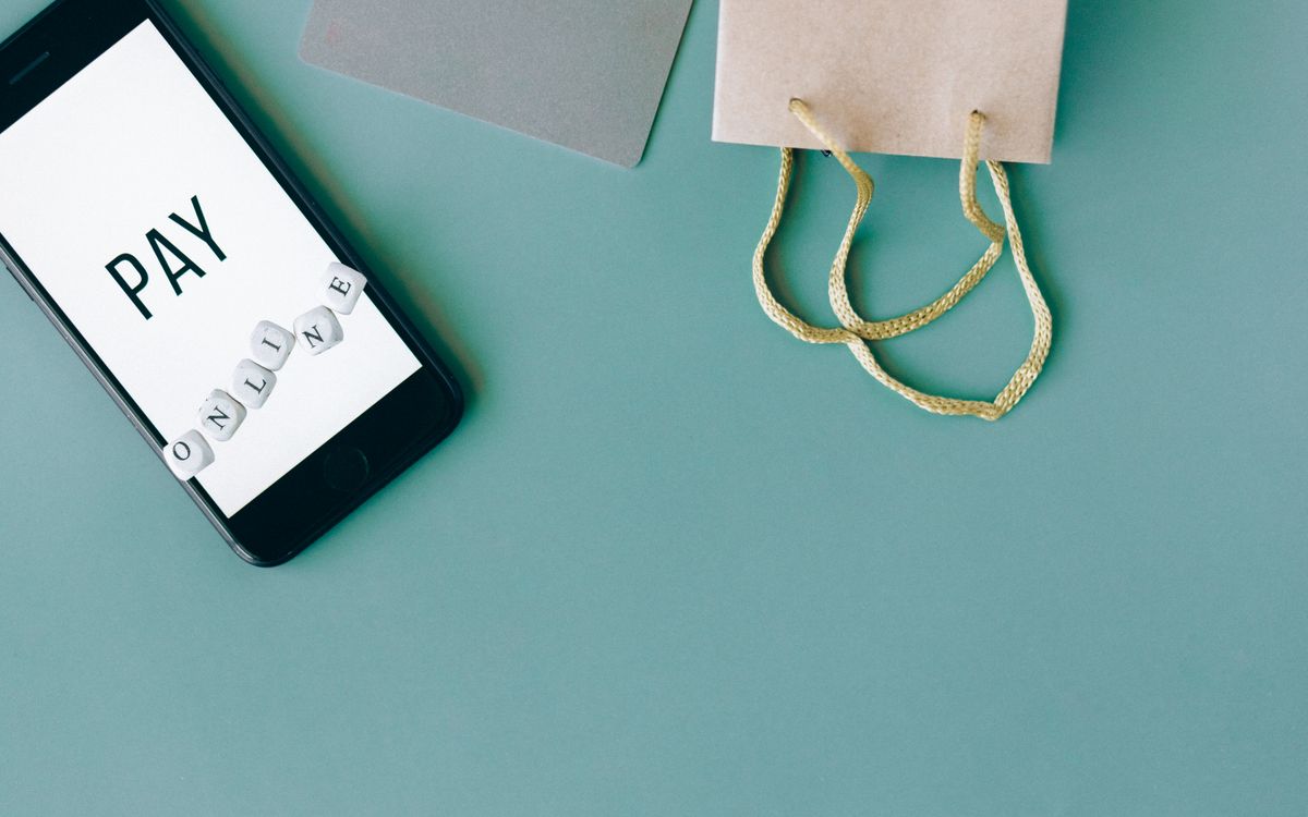 Illustration of online payment with smartphone, credit card, and shopping bag on mint background.