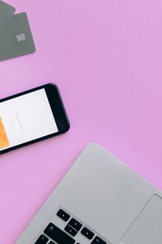 A minimalist top view of a laptop, smartphone, and credit cards on a pink surface.