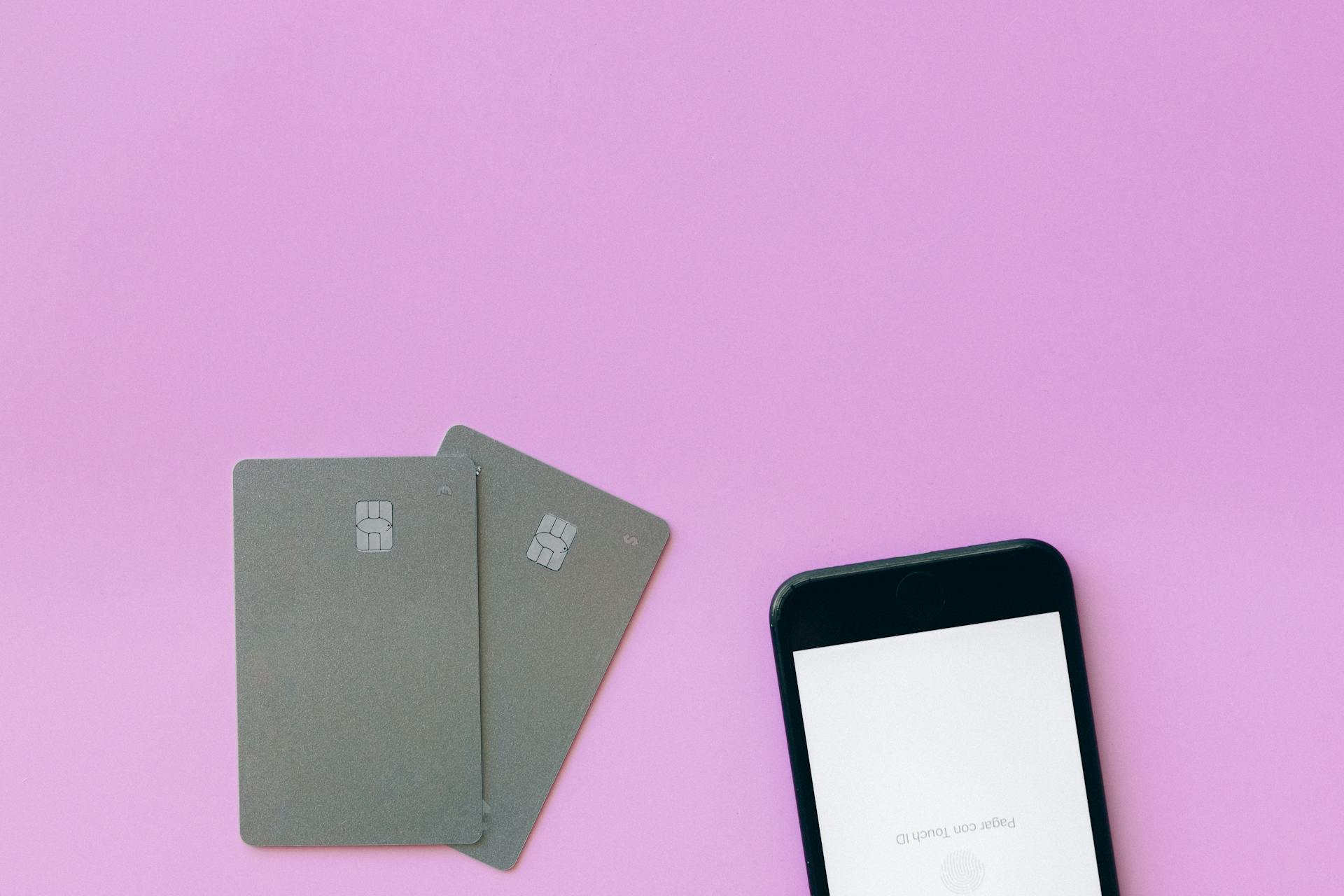 Flat lay of credit cards and smartphone on pink surface, symbolizing digital payment solutions.