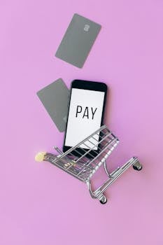 Top view of a smartphone in a shopping cart with credit cards on a purple background.